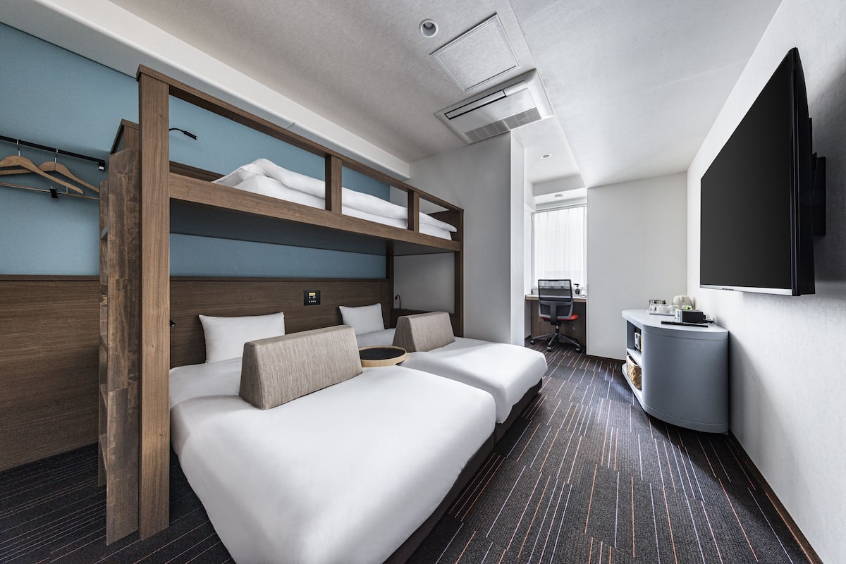 A modern hotel room with a bunk bed, a desk, and a flat-screen TV.