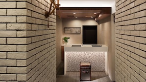 Un espace d’accueil avec un mur en briques, un comptoir d’accueil, un luminaire fixé au mur et une petite plante.