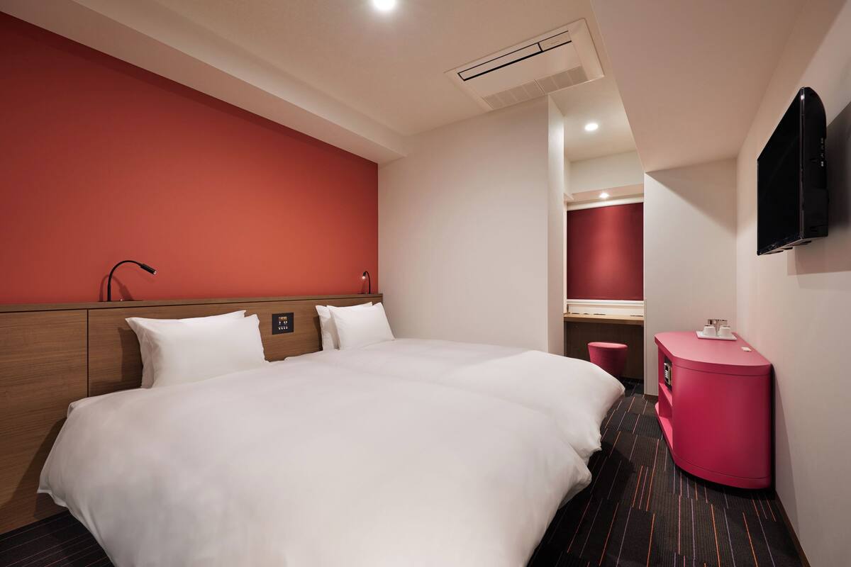 A hotel room with a large bed, a bedside table, a mirror, and a TV mounted on the wall.