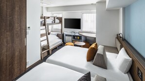 Une chambre d’hôtel moderne équipée de lits superposés, d’un téléviseur à écran plat, d’un bureau avec un ordinateur et d’une fenêtre avec des rideaux.