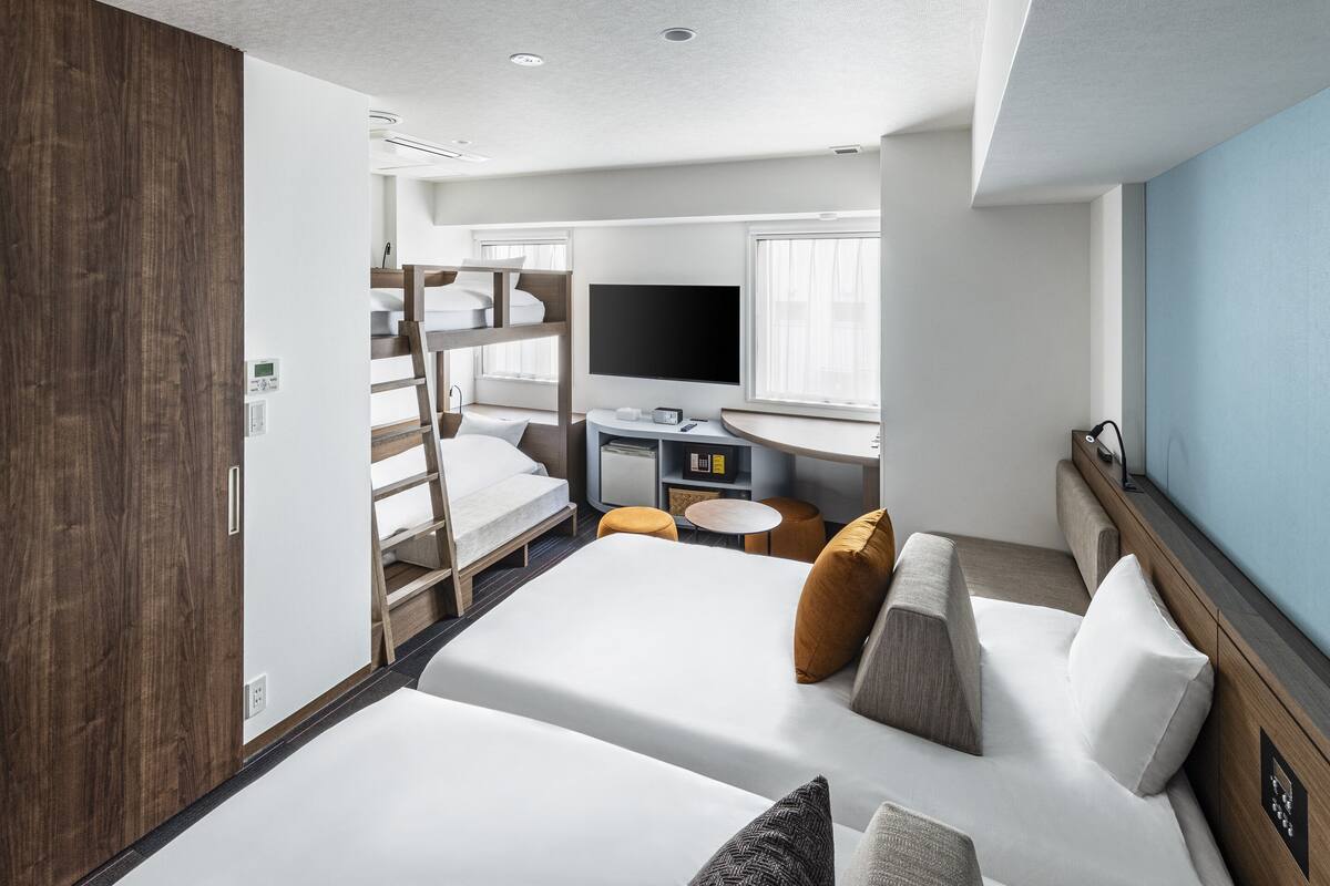 A modern hotel room with bunk beds, a flat-screen TV, a desk with a computer, and a window with curtains.