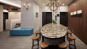 Un espace repas moderne avec une table ronde, six tabourets, un lustre et un mur décoré d’un motif en briques.