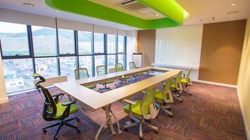 A conference room with a long table, multiple chairs, large windows with a city view, and a modern ceiling design.