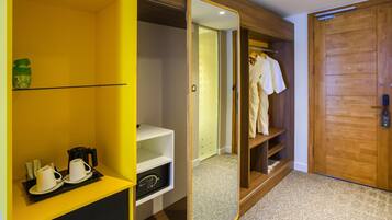 A hotel room with a yellow minibar, a mirror, a wooden wardrobe, and a patterned carpet.