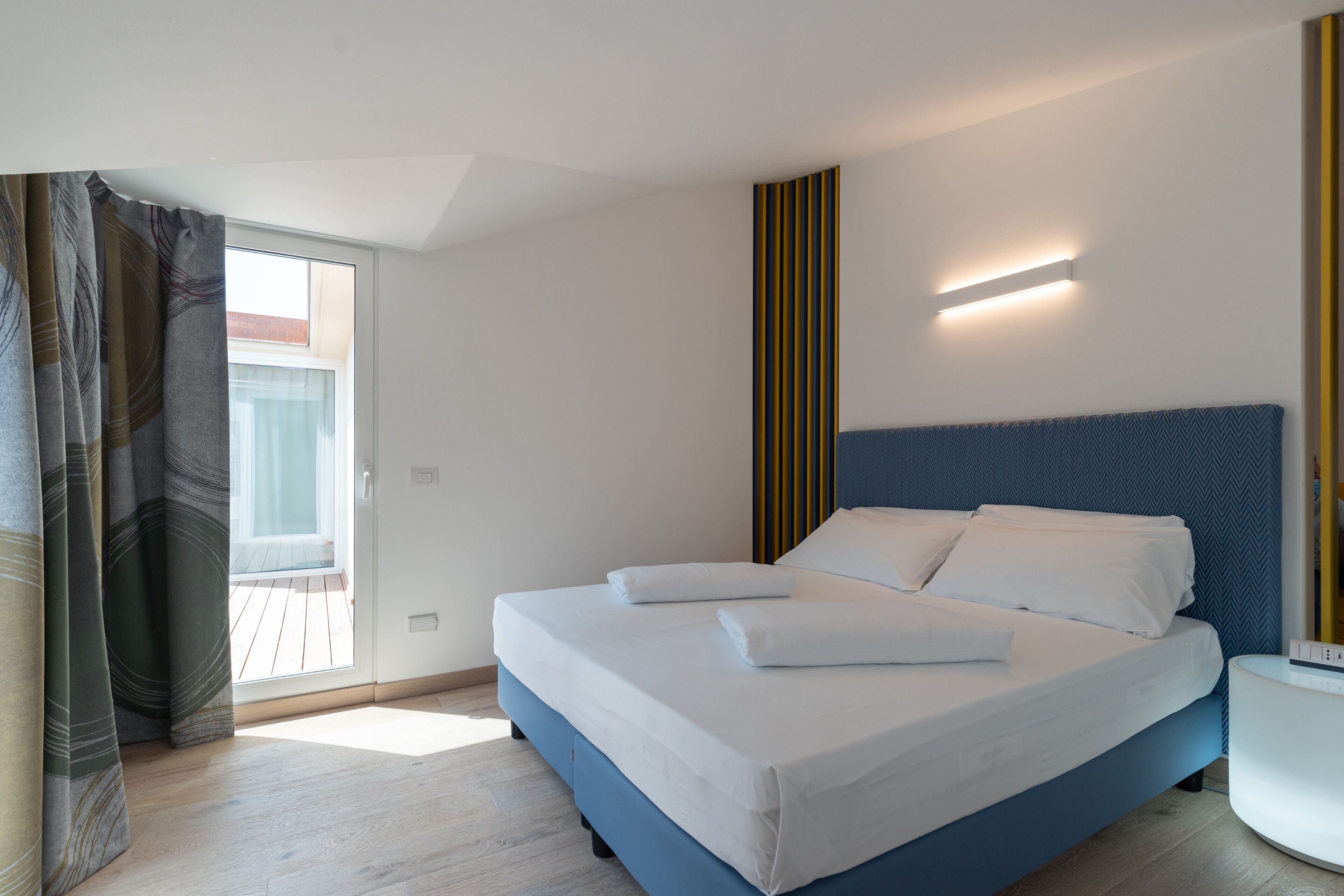 Quarto de hotel moderno com uma cama grande, mesa de cabeceira e vista para a varanda.