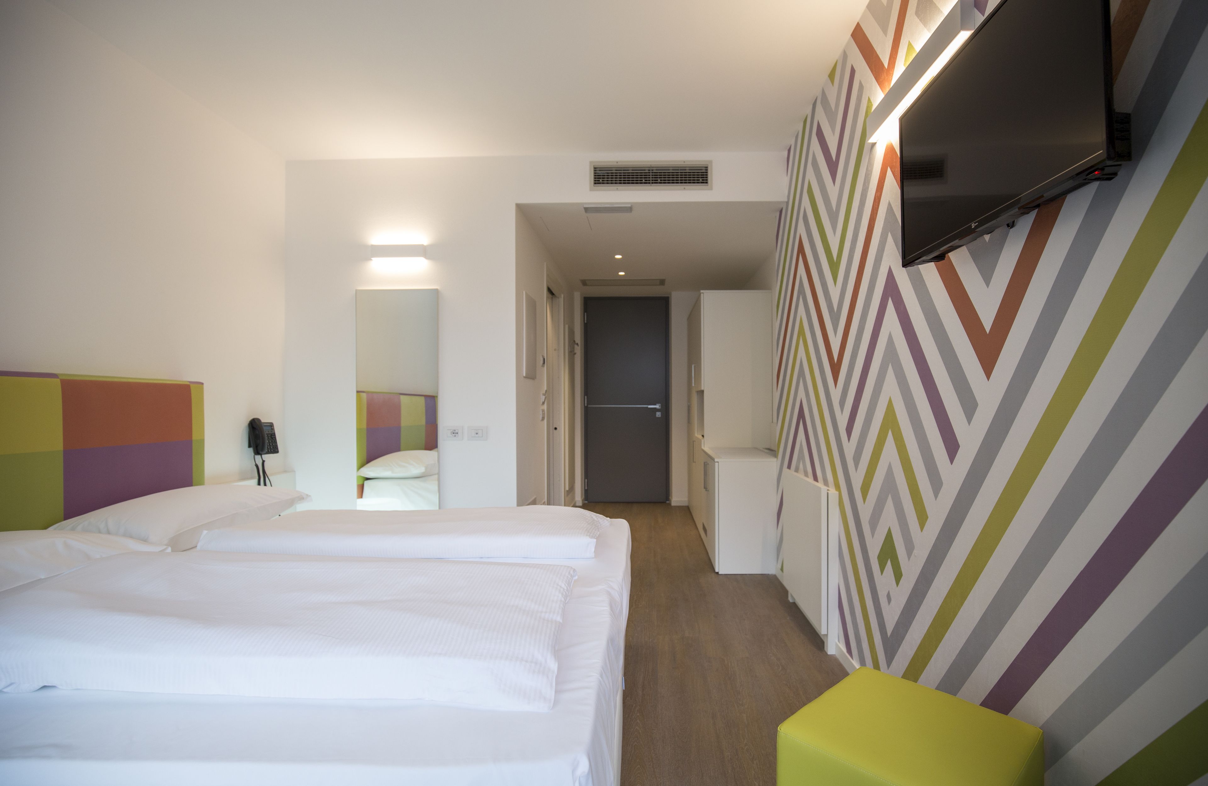 Une chambre d’hôtel équipée d’un lit, d’un bureau, d’une chaise et d’un téléviseur fixé au mur.