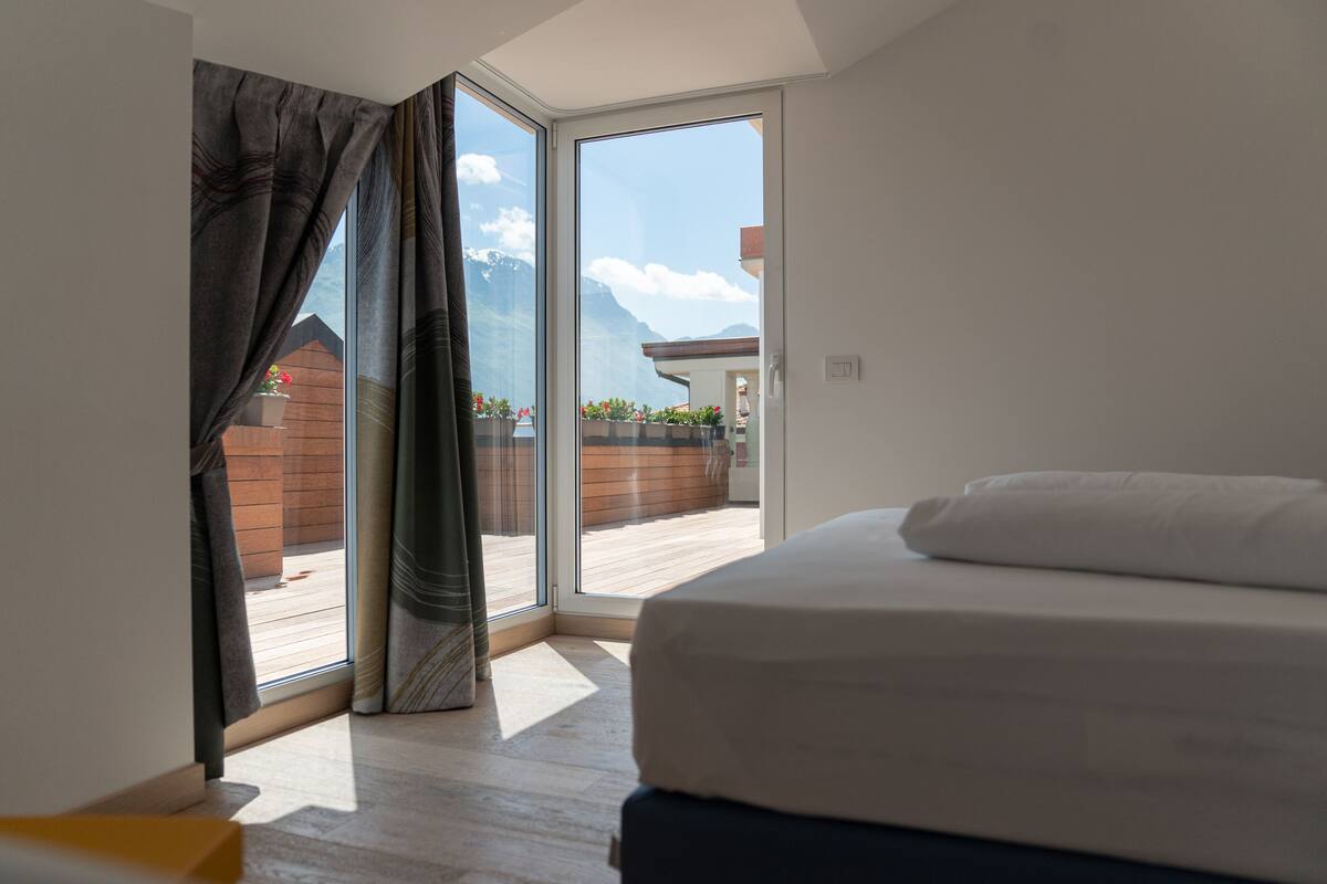 Un dormitorio con un ventanal grande, una cama y vistas a una terraza de madera y montañas.
