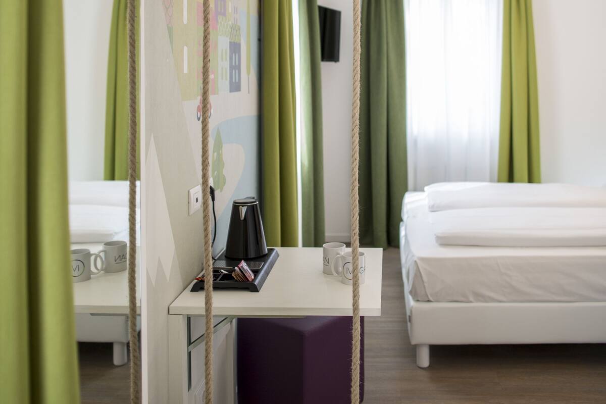 Habitación de hotel con dos camas, un escritorio con silla, un columpio colgante y un televisor montado en la pared.