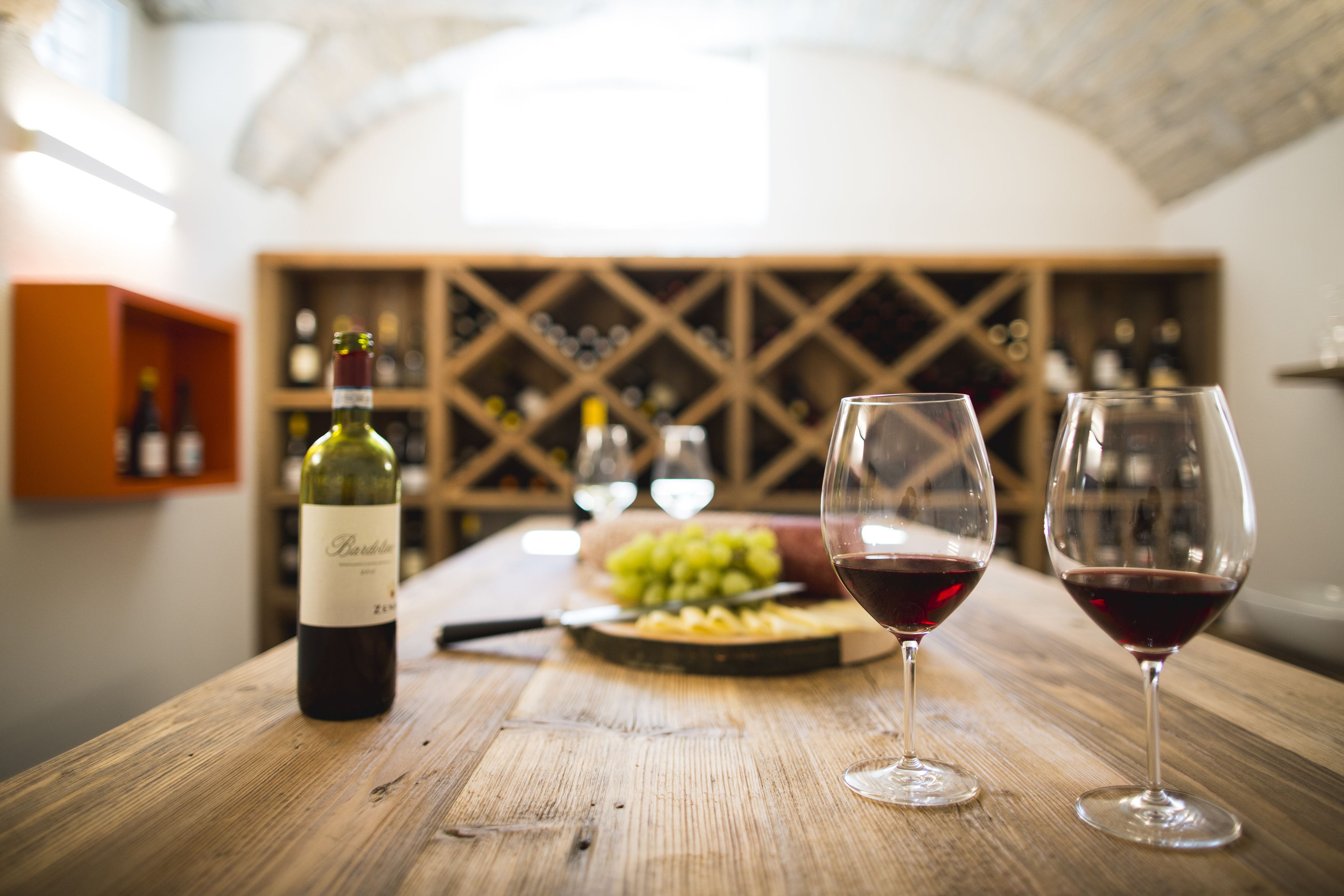 A wooden table with a bottle of wine, two glasses of red wine, and a bowl of grapes.