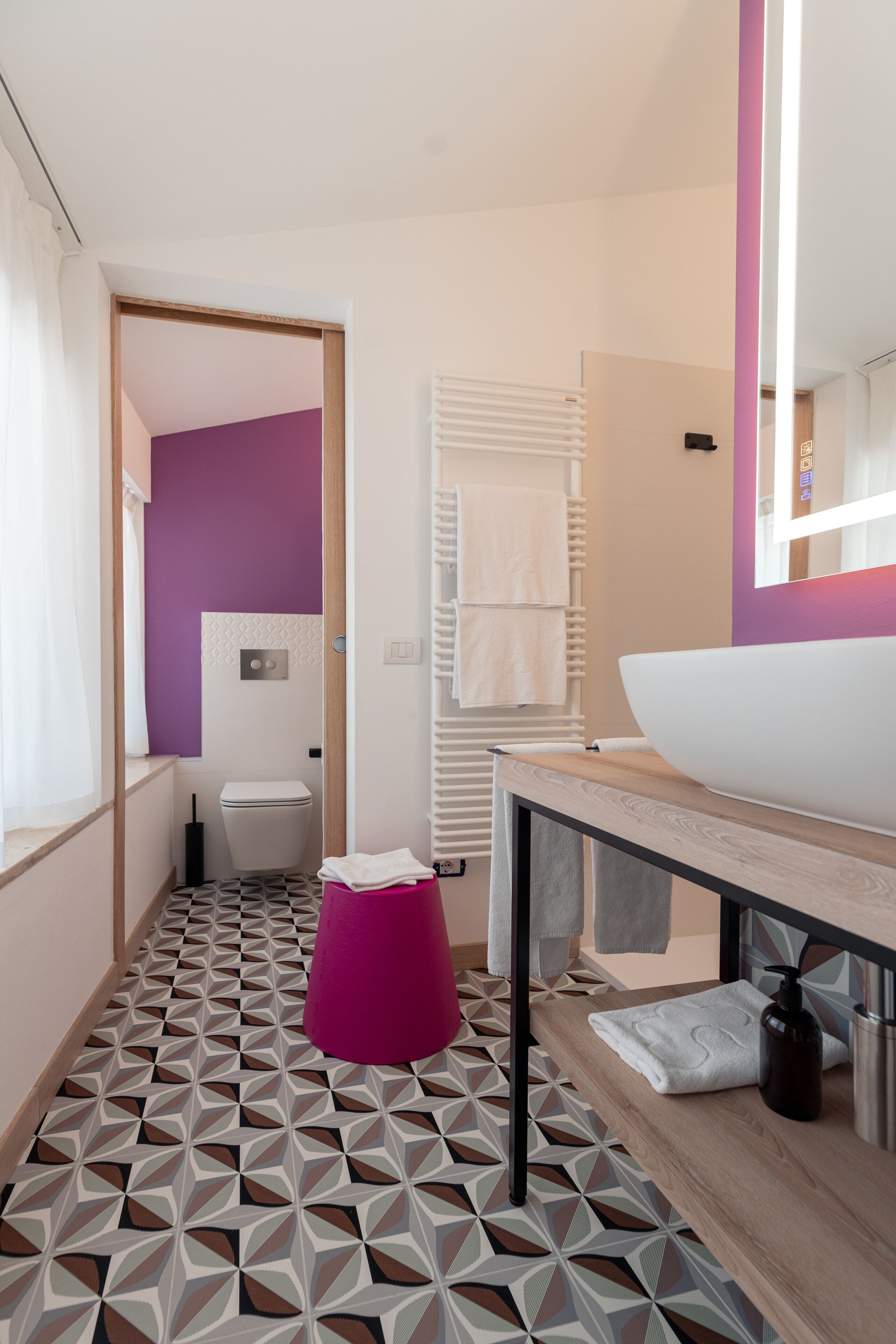 A bathroom with a geometric patterned floor, a purple stool, a white sink, and a mirror with a purple frame.