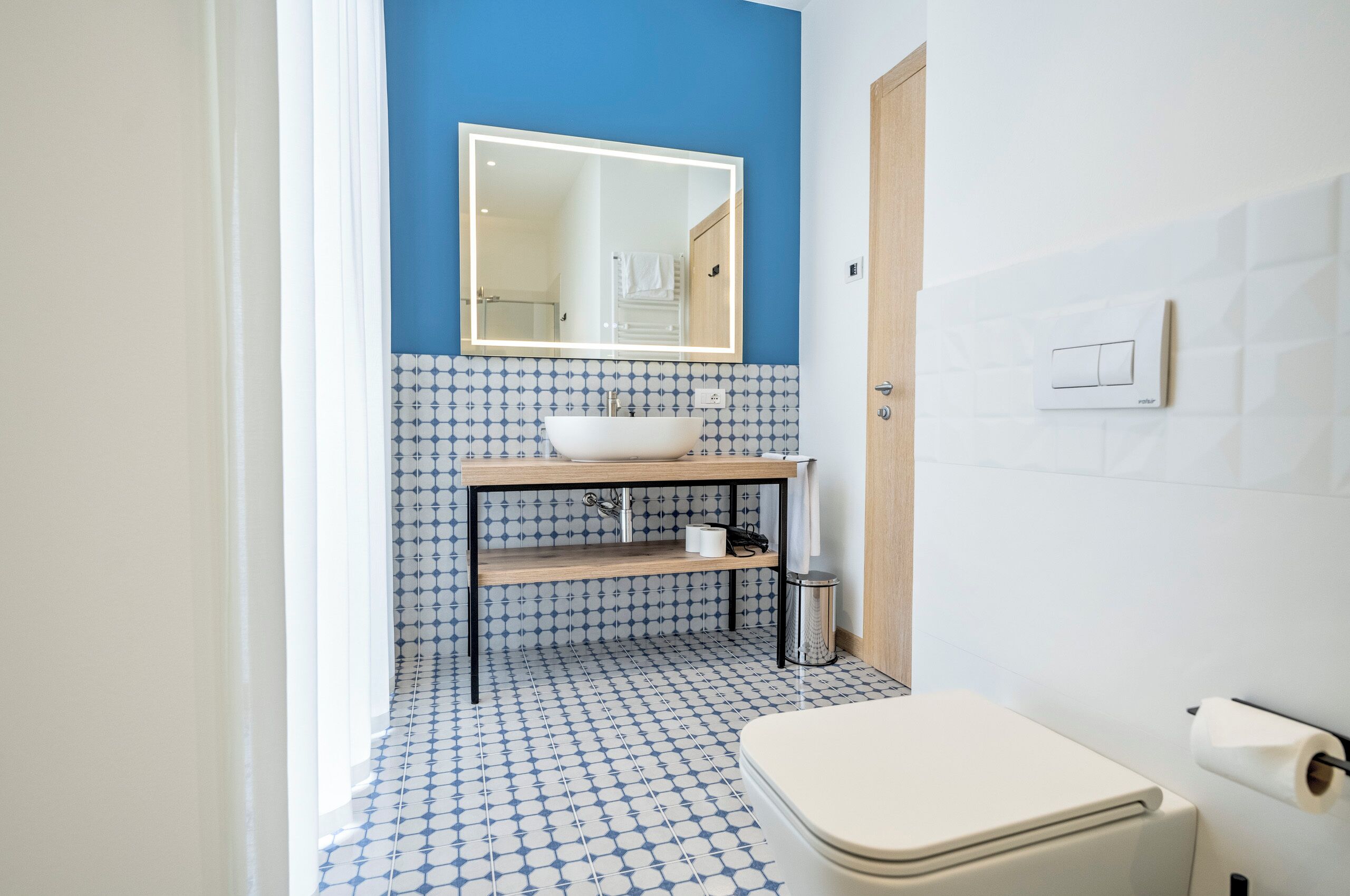 A bathroom with a white toilet, a sink with a mirror above it, and a blue and white patterned floor.