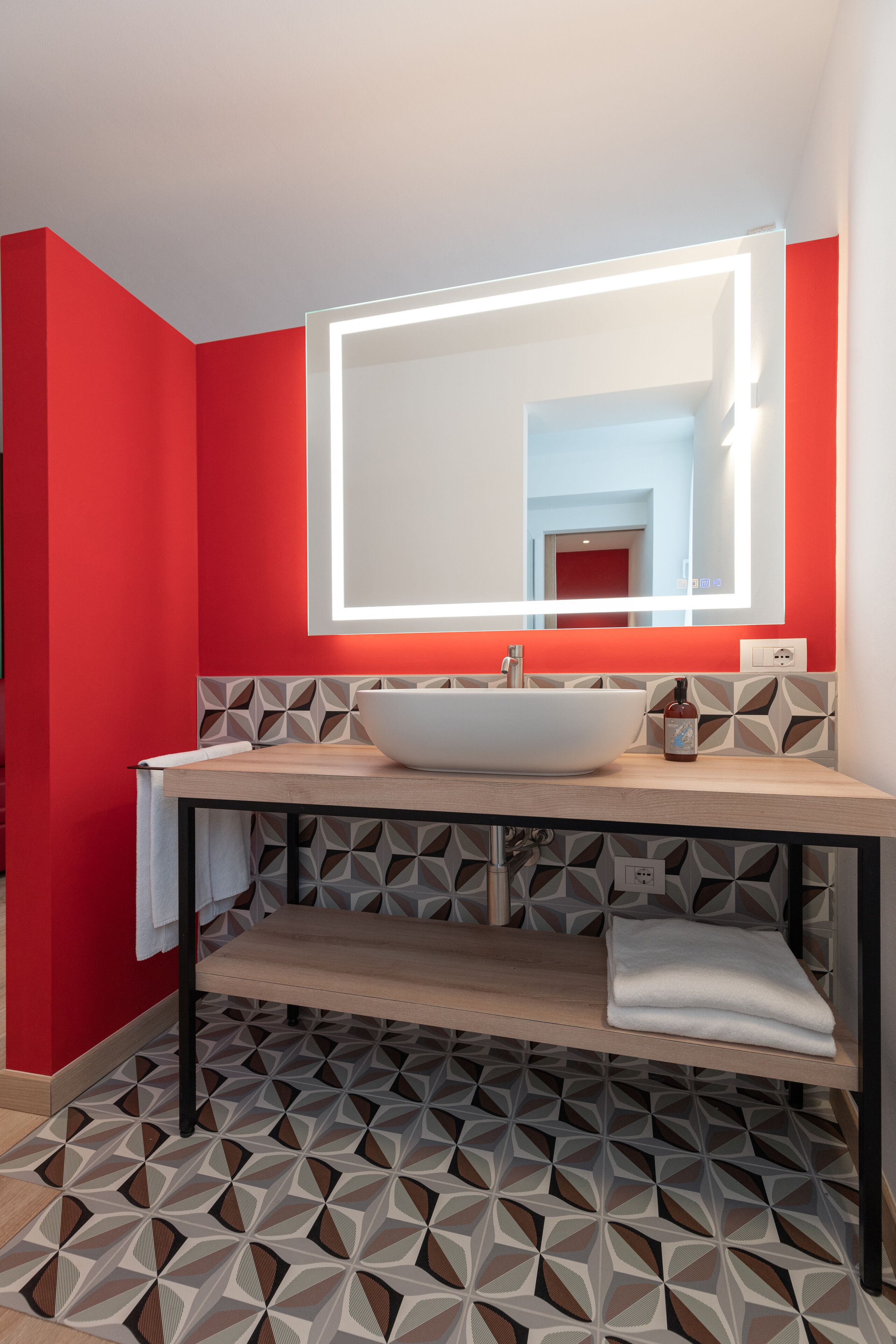A modern bathroom with a geometric patterned floor, a white sink, and a mirror with a lighted frame.