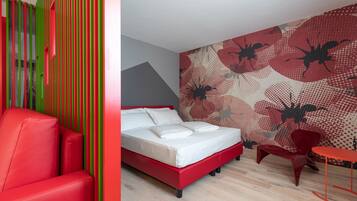 A modern hotel room with a red bed, a red chair, a red table, and a colorful striped wall.