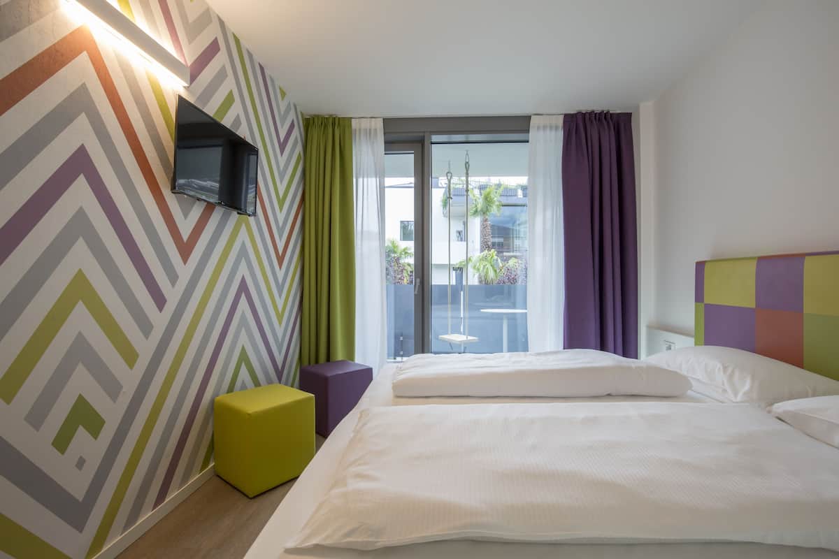 Habitación de hotel con cama, televisión en la pared, ventana con cortinas y vistas al exterior.