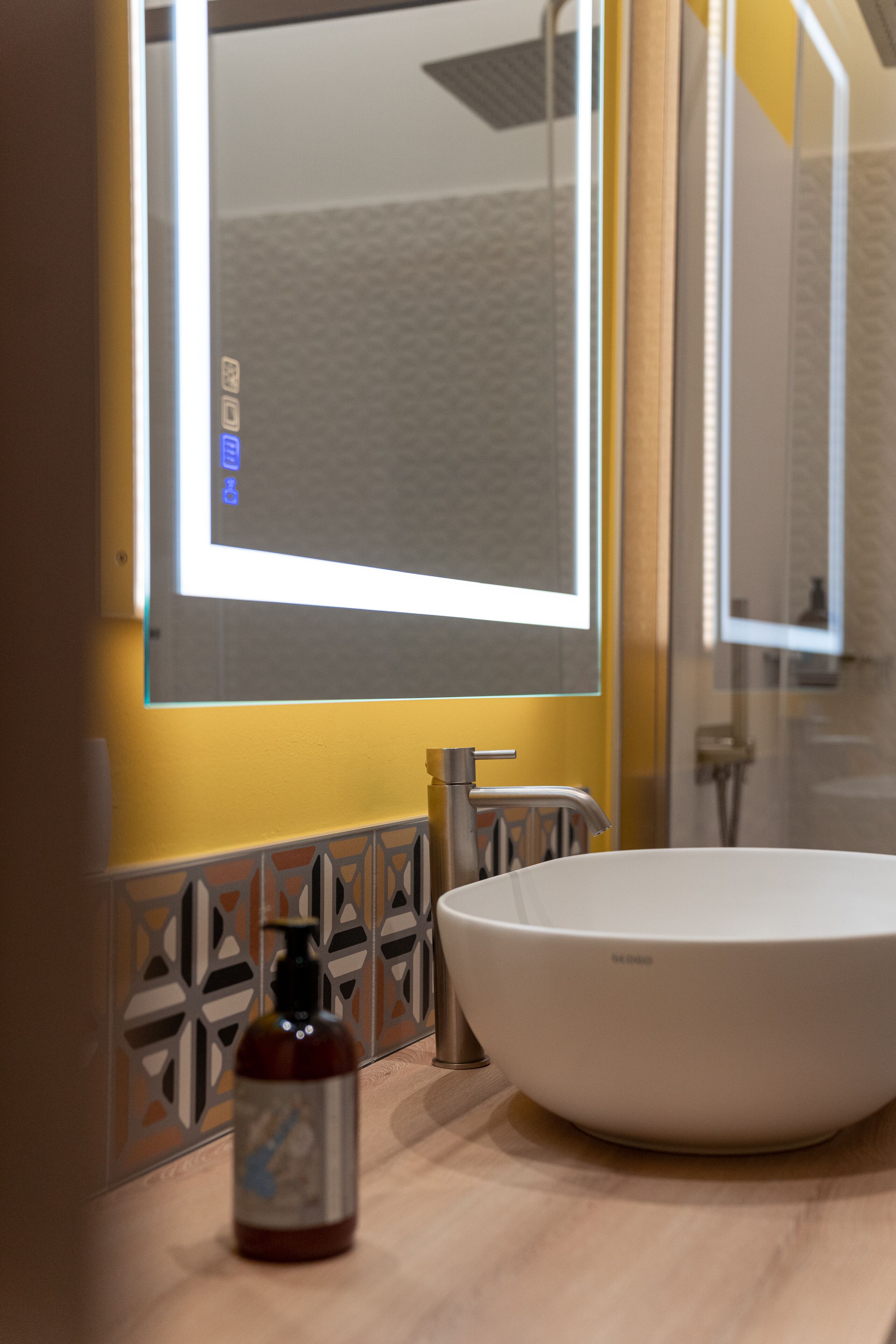 Une salle de bain avec un lavabo blanc, un miroir et un flacon de savon pour les mains.