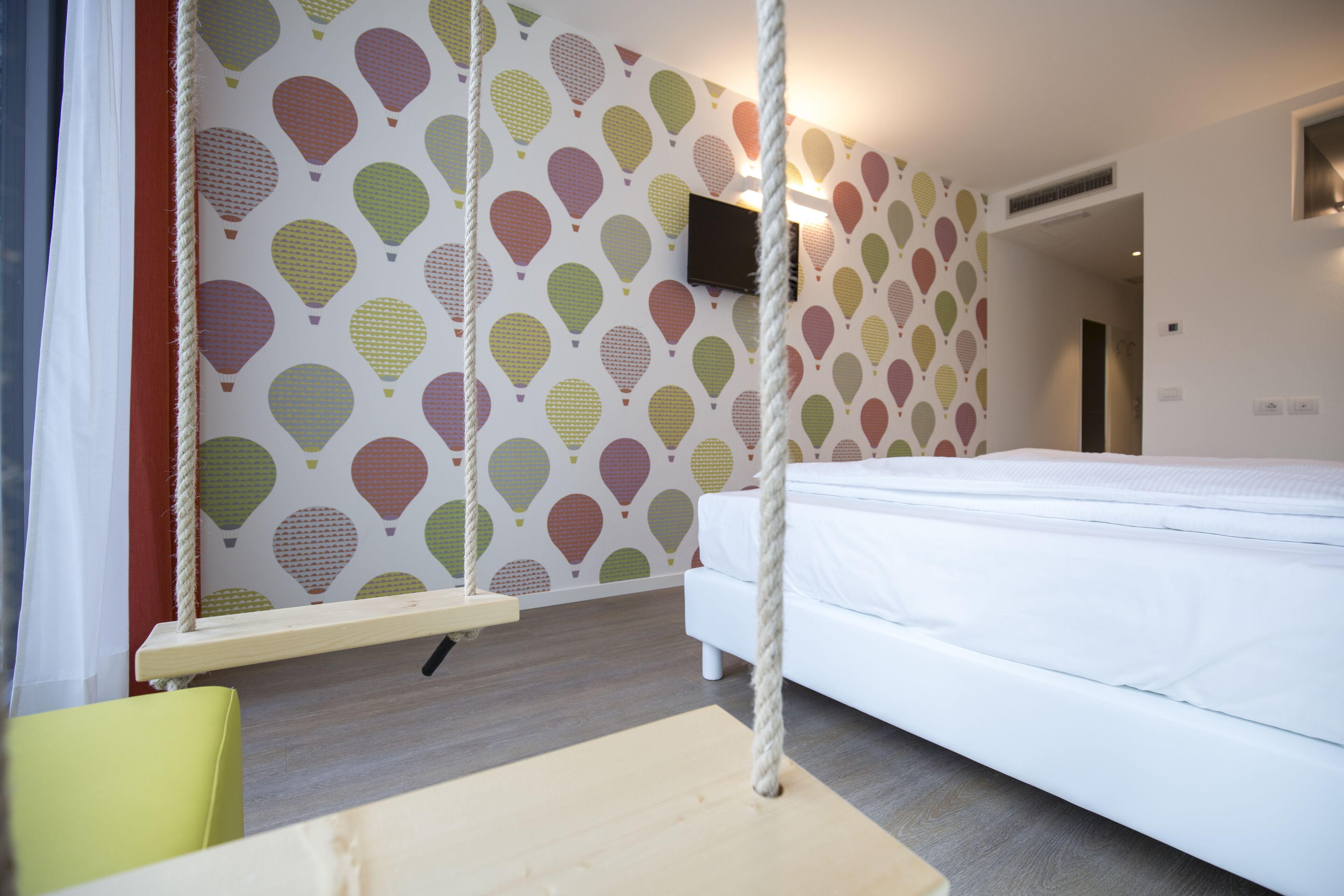 Un dormitorio con una cama, un columpio colgante y una pared con diseño de globo aerostático.