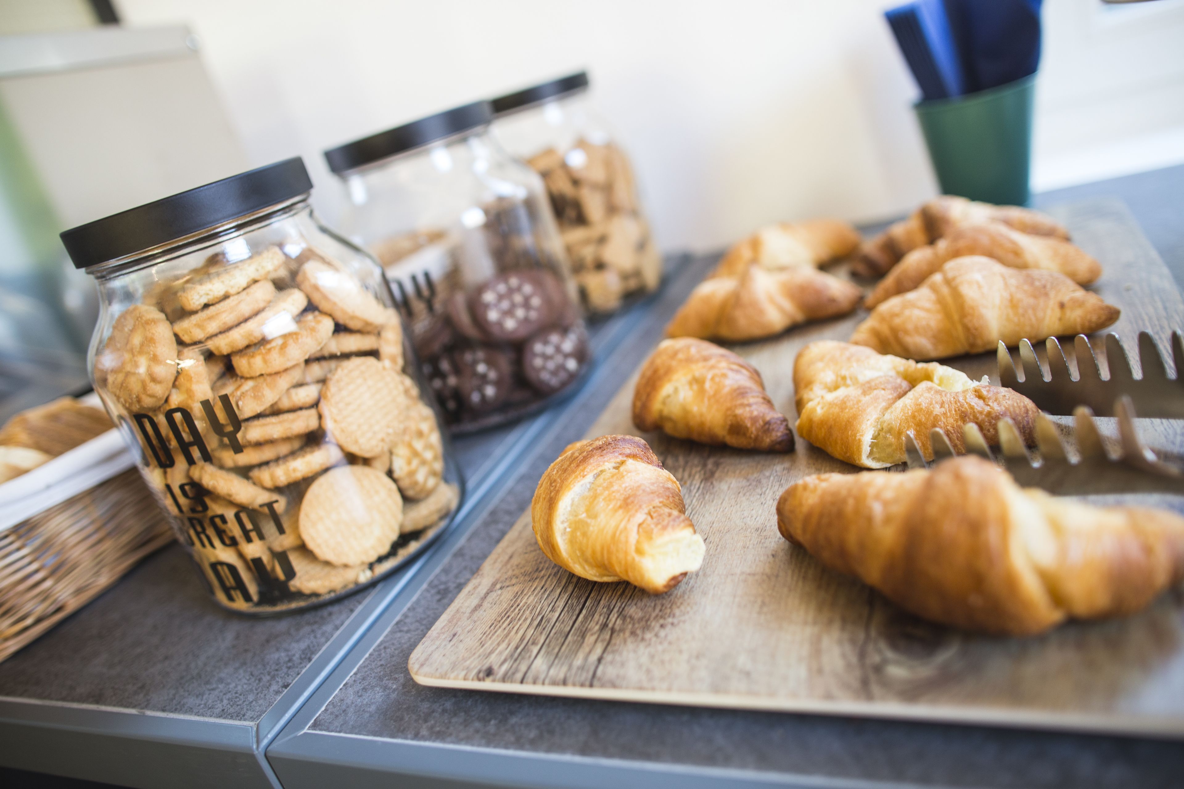 A wooden cutting board with croissants and a jar of cookies.