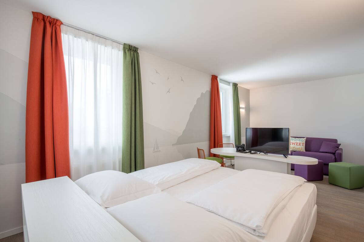 Una habitación de hotel con dos camas, un escritorio, una silla, un sofá y un televisor.