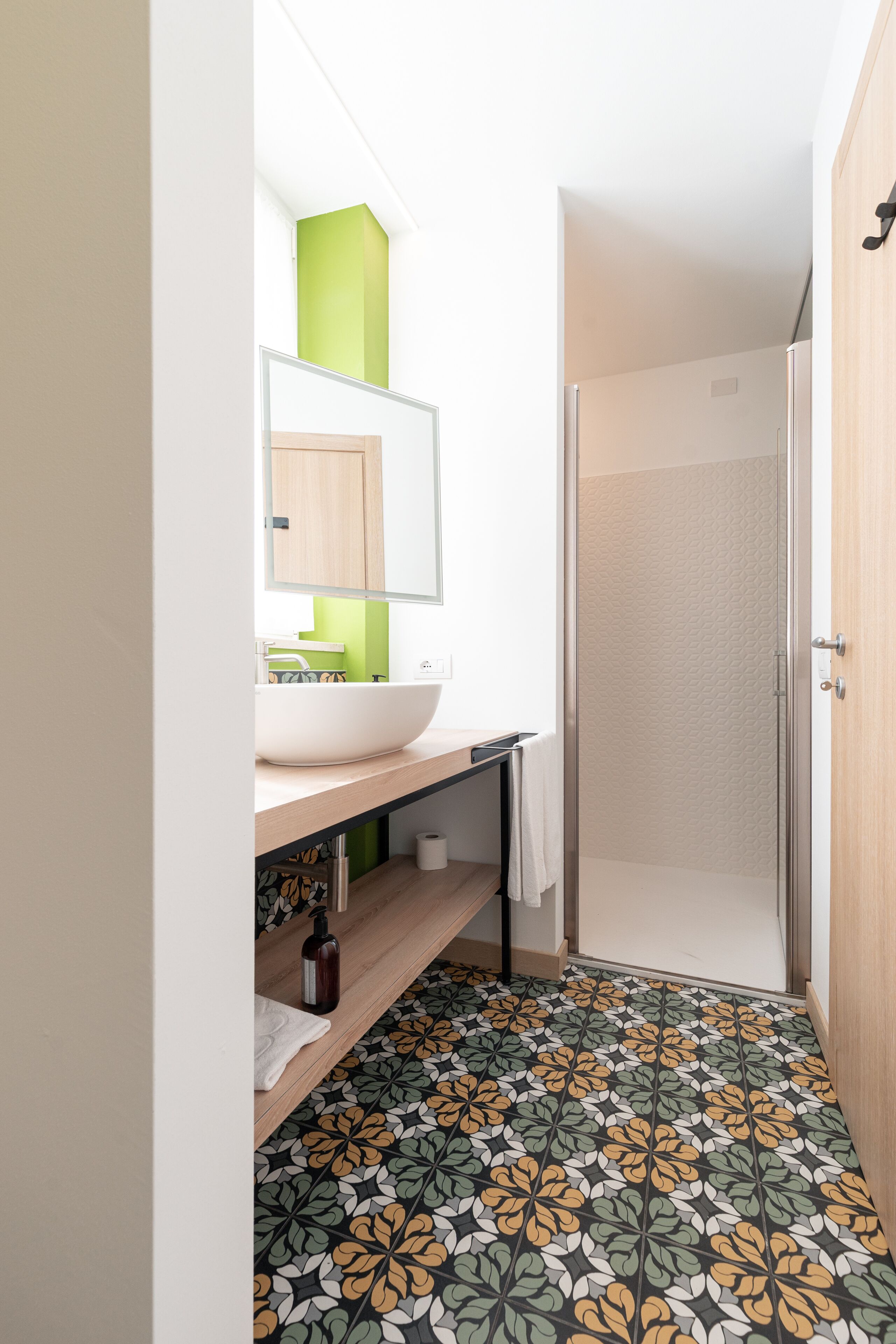 A bathroom with a white sink, green accent wall, patterned floor tiles, and a shower area.