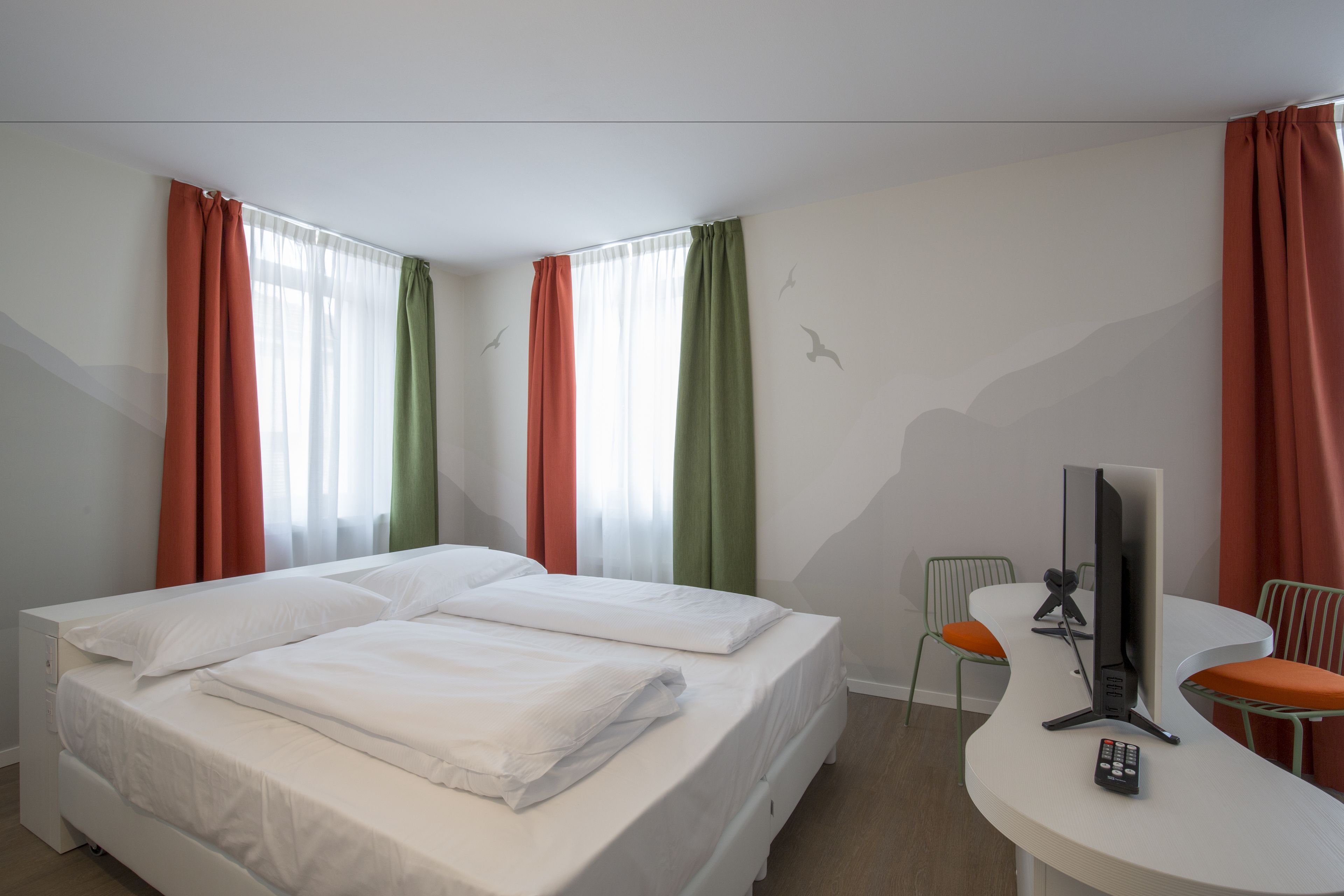 Hotellihuone, jossa on sänky, työpöytä, tuoli ja televisio.