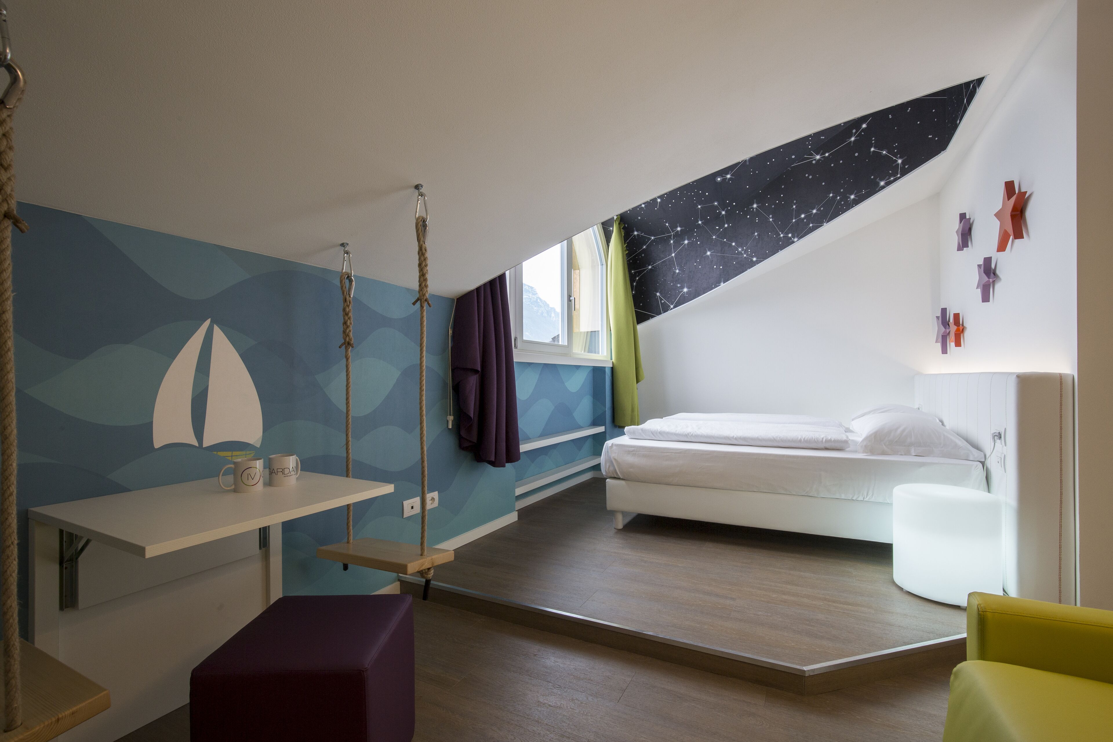 A bedroom with a bed, a desk, a hanging chair, and a window with curtains.