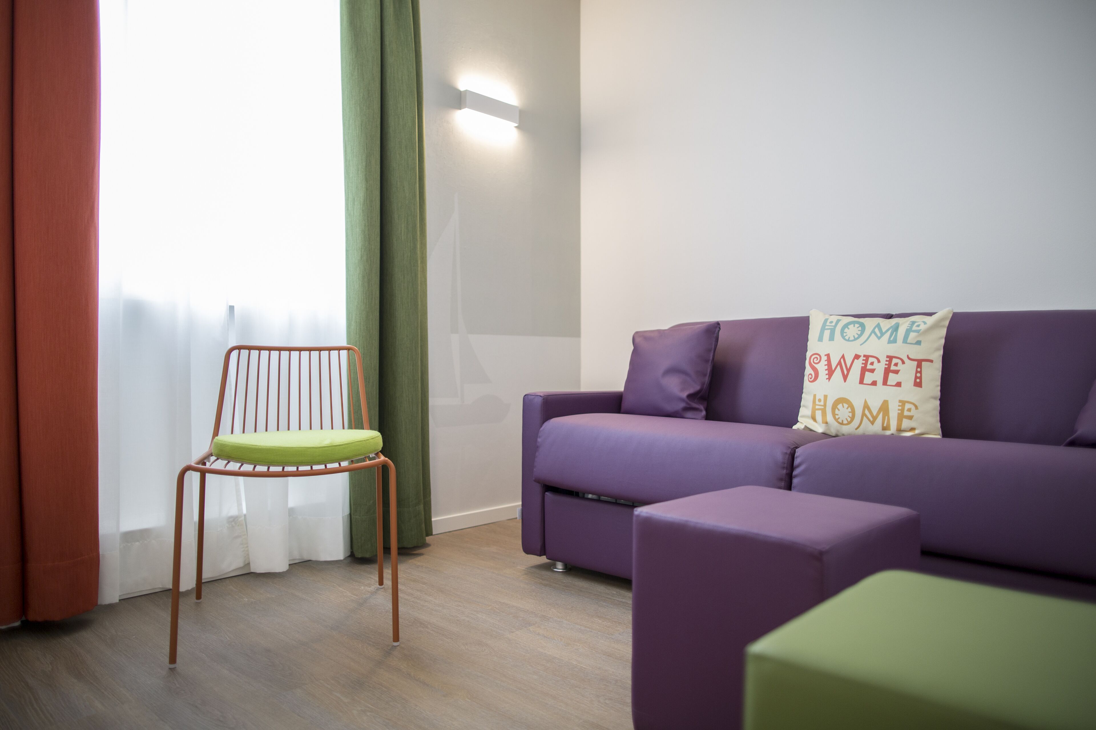 Een moderne woonkamer met een paarse bank, een groene fauteuil en een kussen met de tekst 'HOME SWEET HOME'.