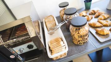 Een keukenhoek met een broodrooster, potten met spreads en een schaal met brood.