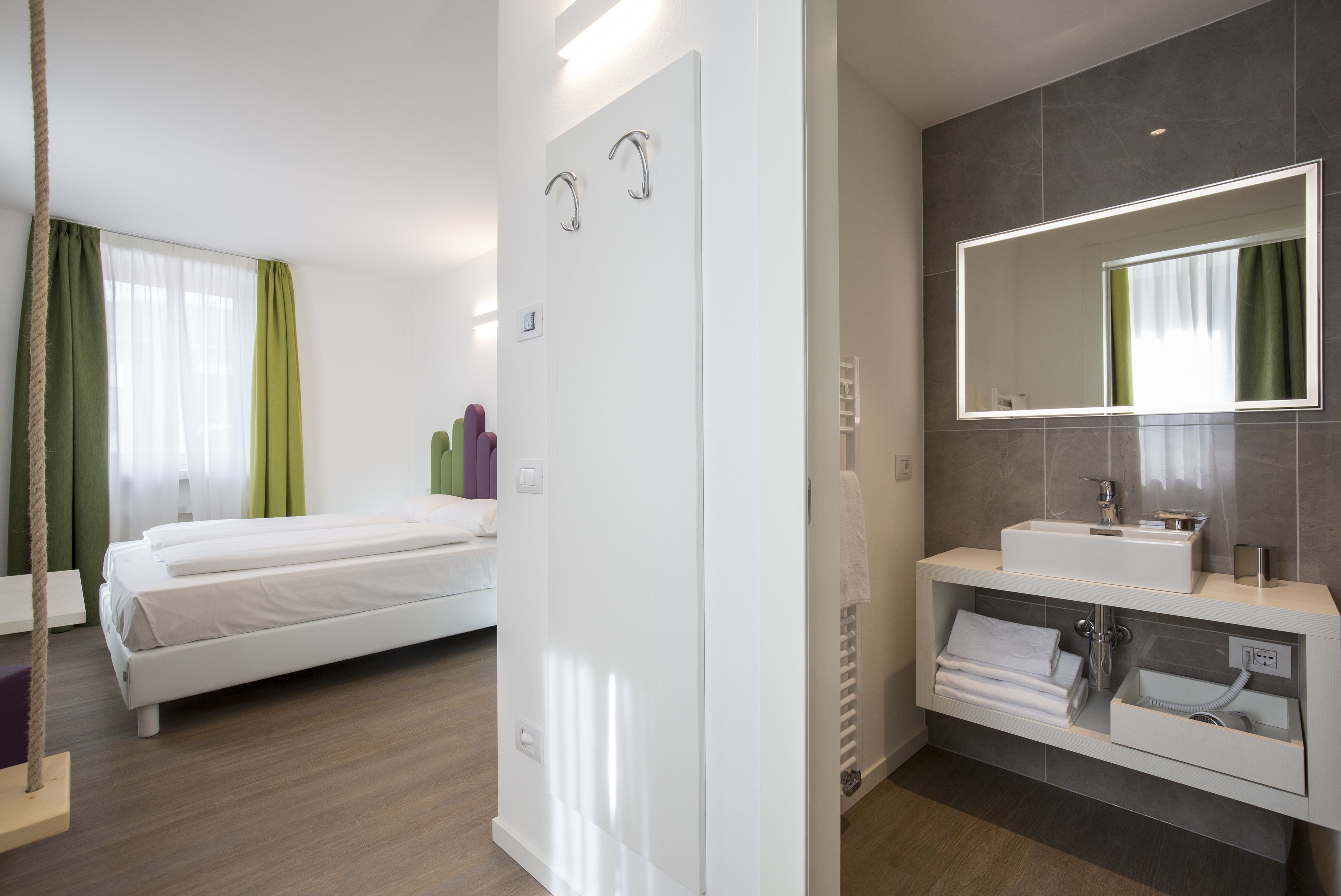 Une chambre d’hôtel moderne, équipée d’un lit, d’une salle de bain avec un miroir et d’une armoire blanche.