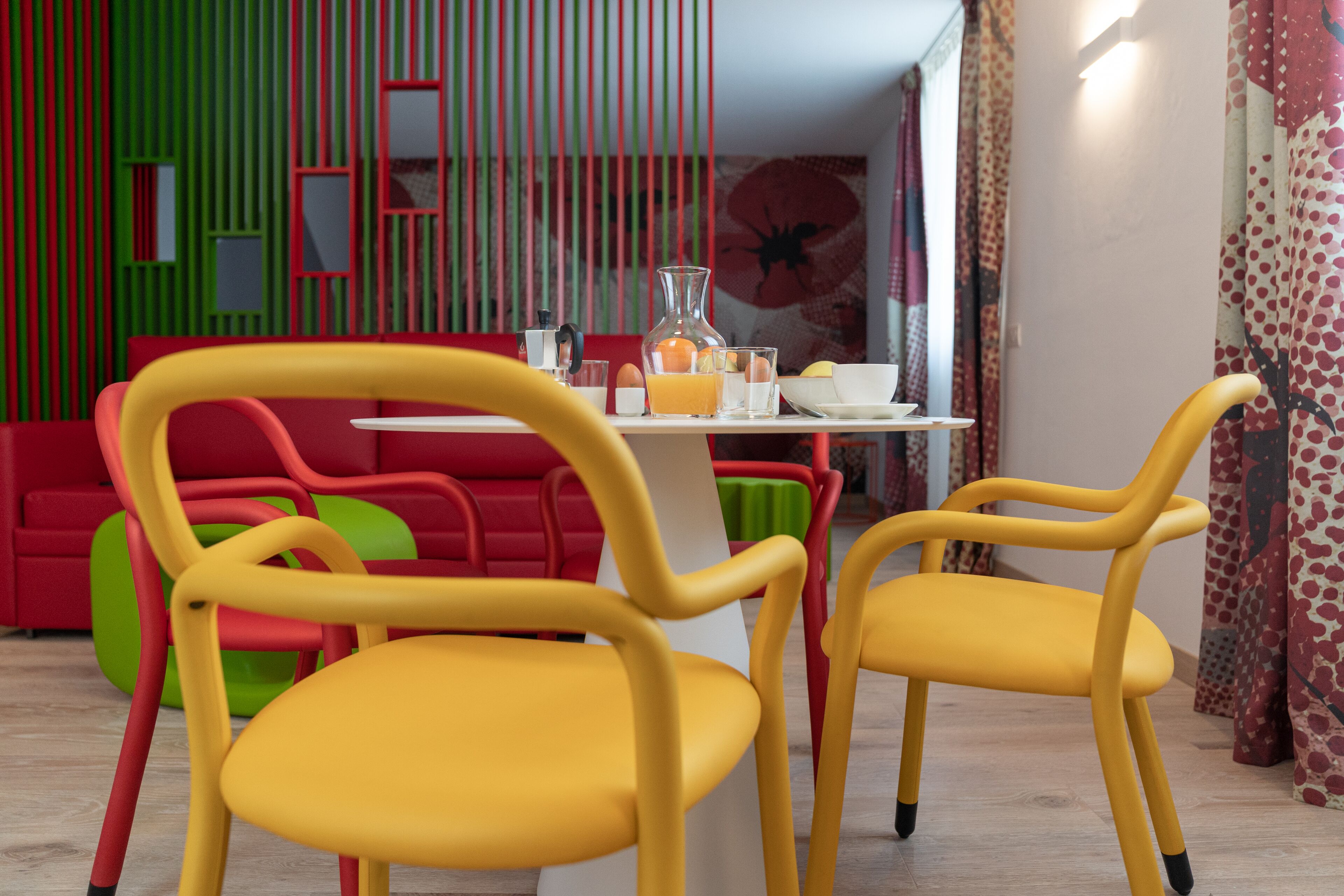 Un área de comedor con sillas amarillas, una mesa blanca y un fondo rojo y verde.
