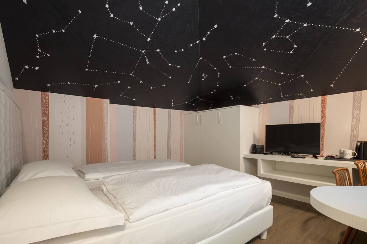 Habitación de hotel con dos camas, un escritorio con televisor y una mesita pequeña.
