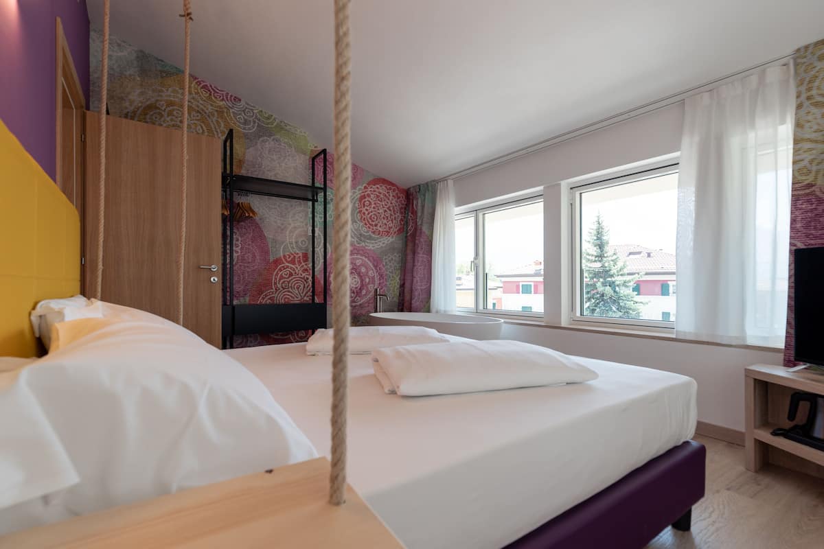 Un dormitorio con cama, armario de madera, televisor y ventana con vista a edificios.