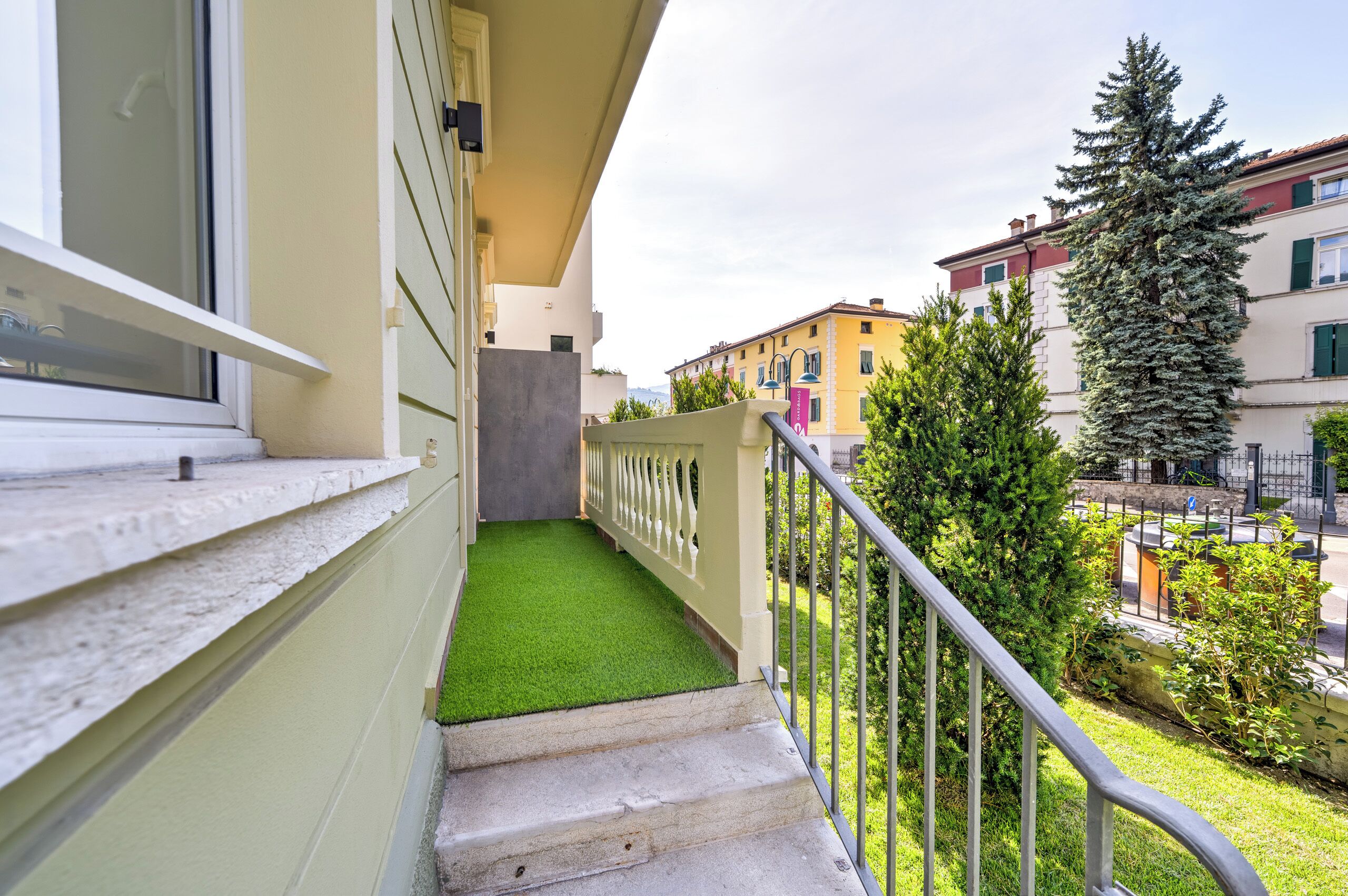A residential building with a balcony, a small grassy area, and a view of neighboring buildings.