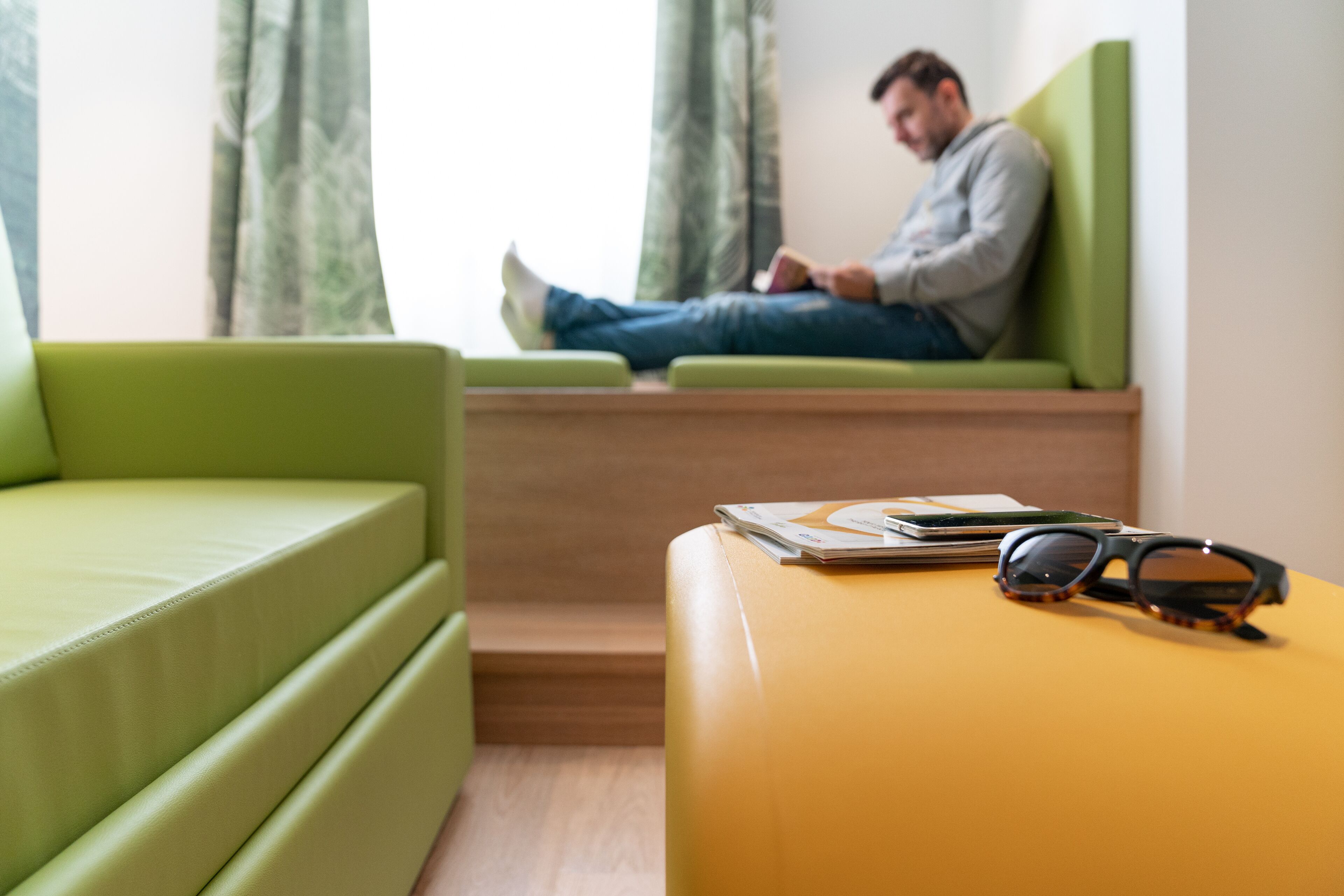 Une pièce avec un canapé vert, un pouf jaune et une paire de lunettes de soleil posée sur le pouf.