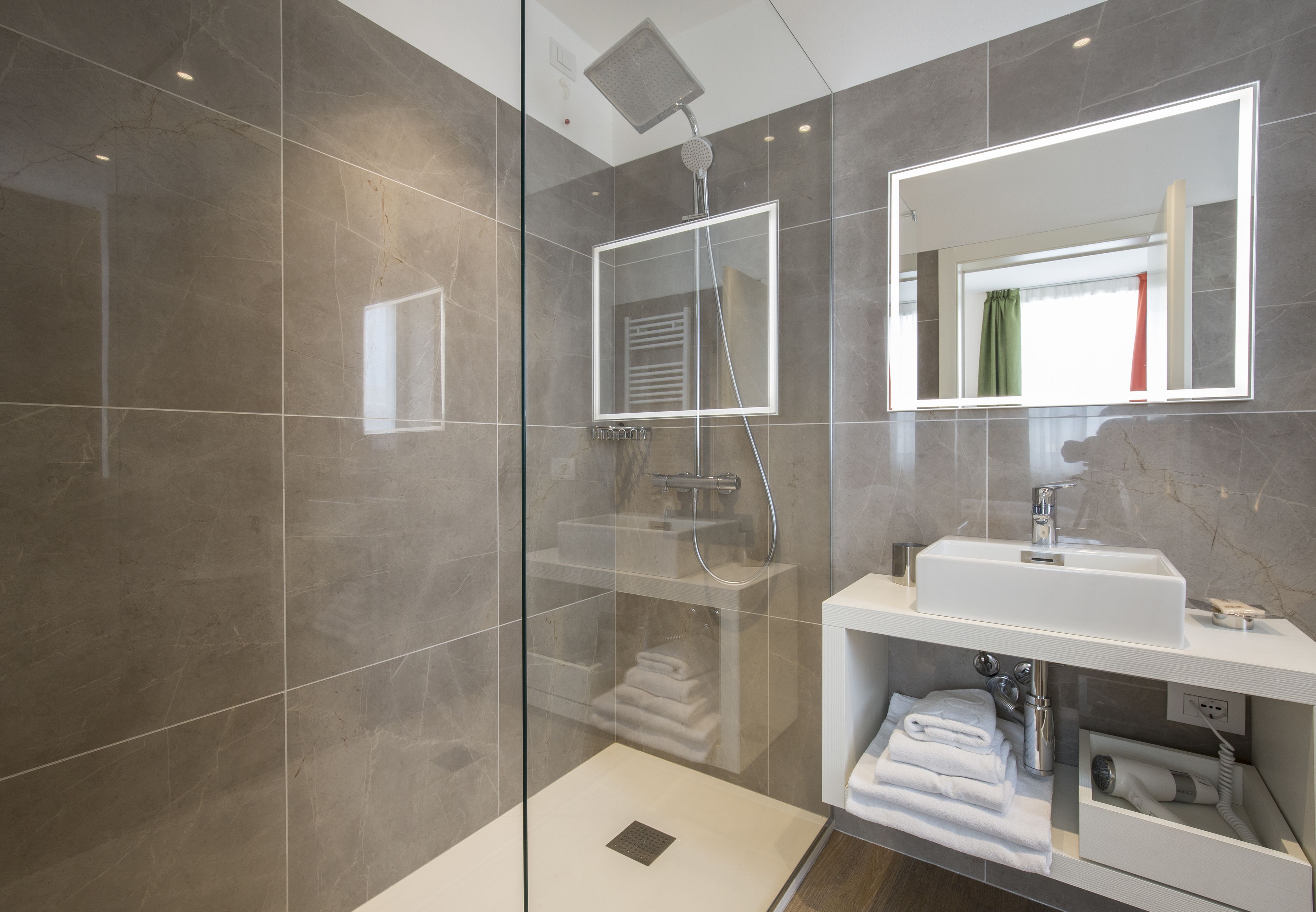 Une salle de bain moderne avec une douche à parois de verre, un lavabo blanc et un miroir au-dessus.