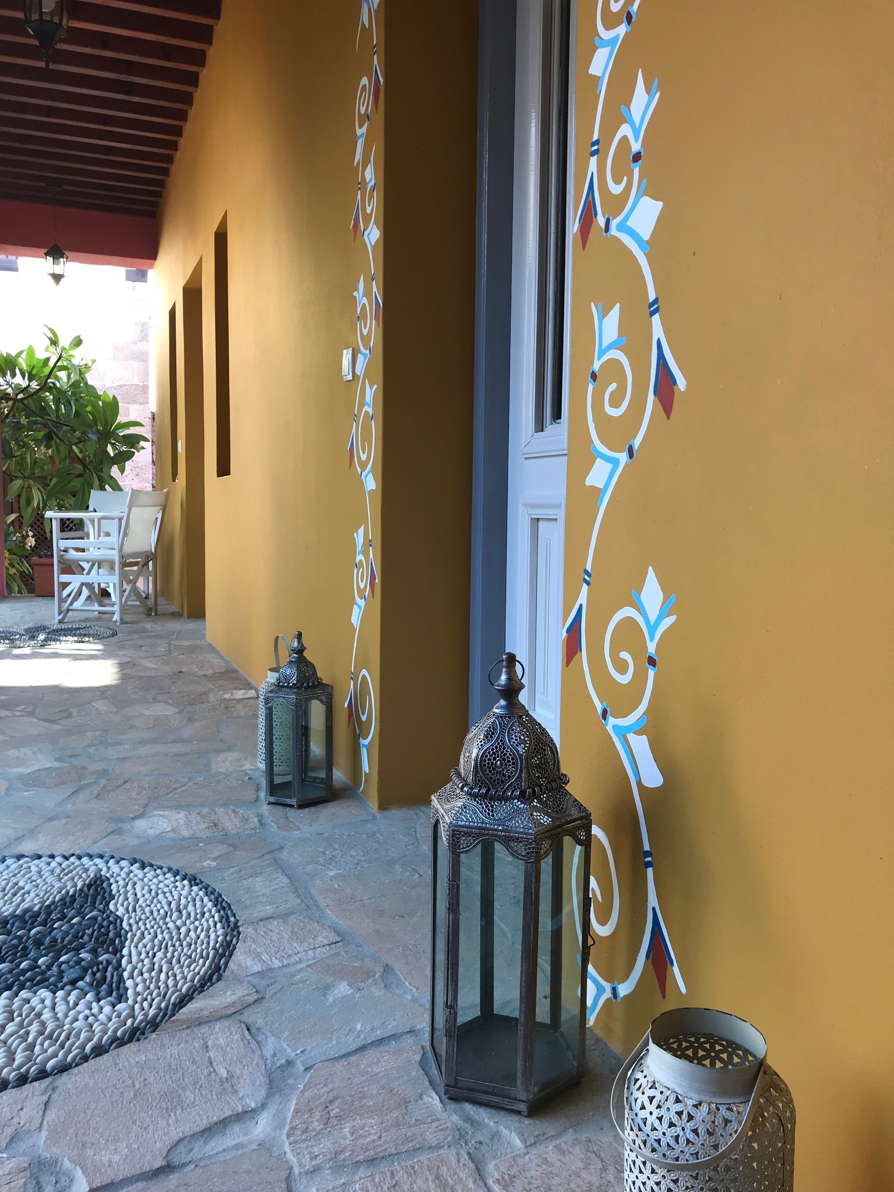 Un patio al aire libre con pared amarilla, barandillas de metal decorativas y dos faroles.