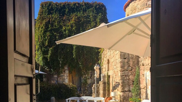 Un umbral abierto a un patio con mobiliario exterior, una estatua y un muro de piedra.