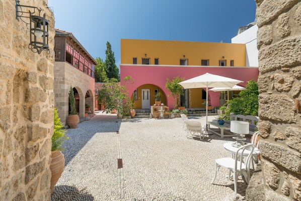 Un patio con suelo de piedra, mobiliario exterior y un edificio de fachada amarilla.