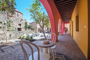 Un patio con suelo de piedra, sillas blancas y una mesa con cojín.