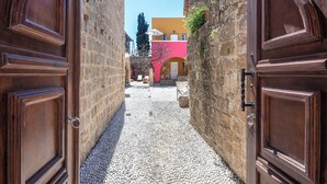 Un estrecho callejón con suelo de adoquines, flanqueado por muros de piedra y puertas de madera.