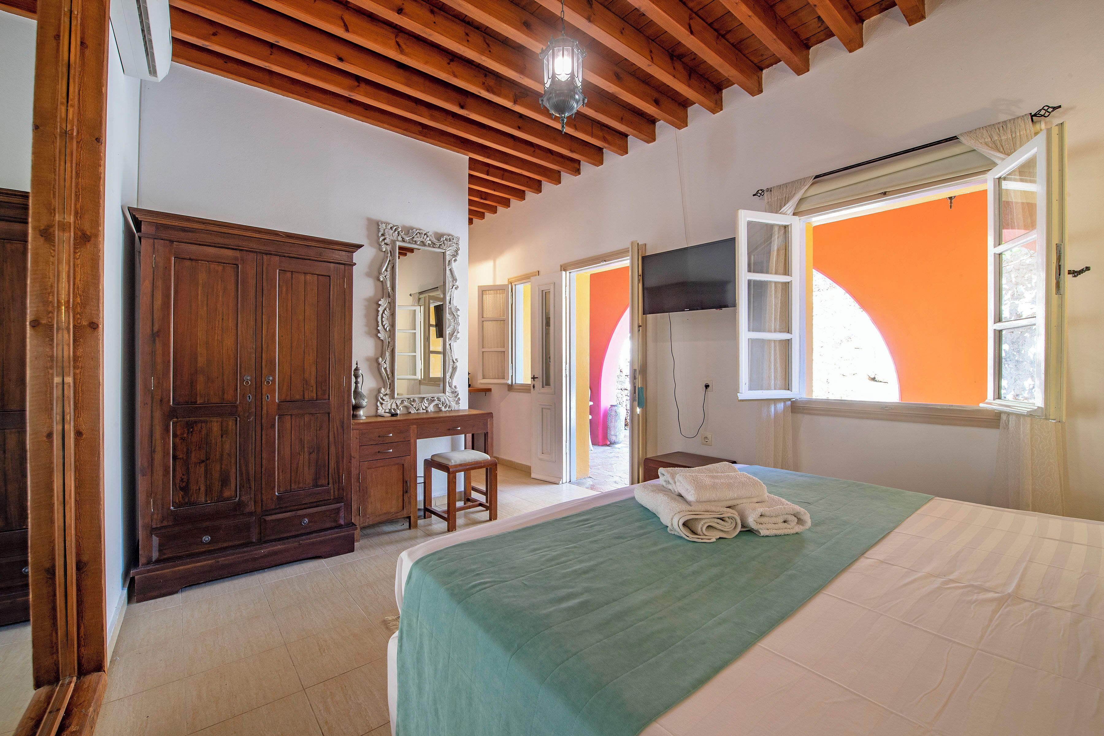Une chambre à coucher comprenant un lit, une armoire en bois, un bureau, une chaise, un miroir et un téléviseur.