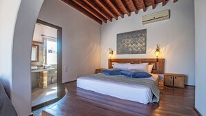 Un dormitorio con techo de madera, una cama con colcha a rayas blancas y azules, dos lámparas de noche y un pequeño armario de madera.