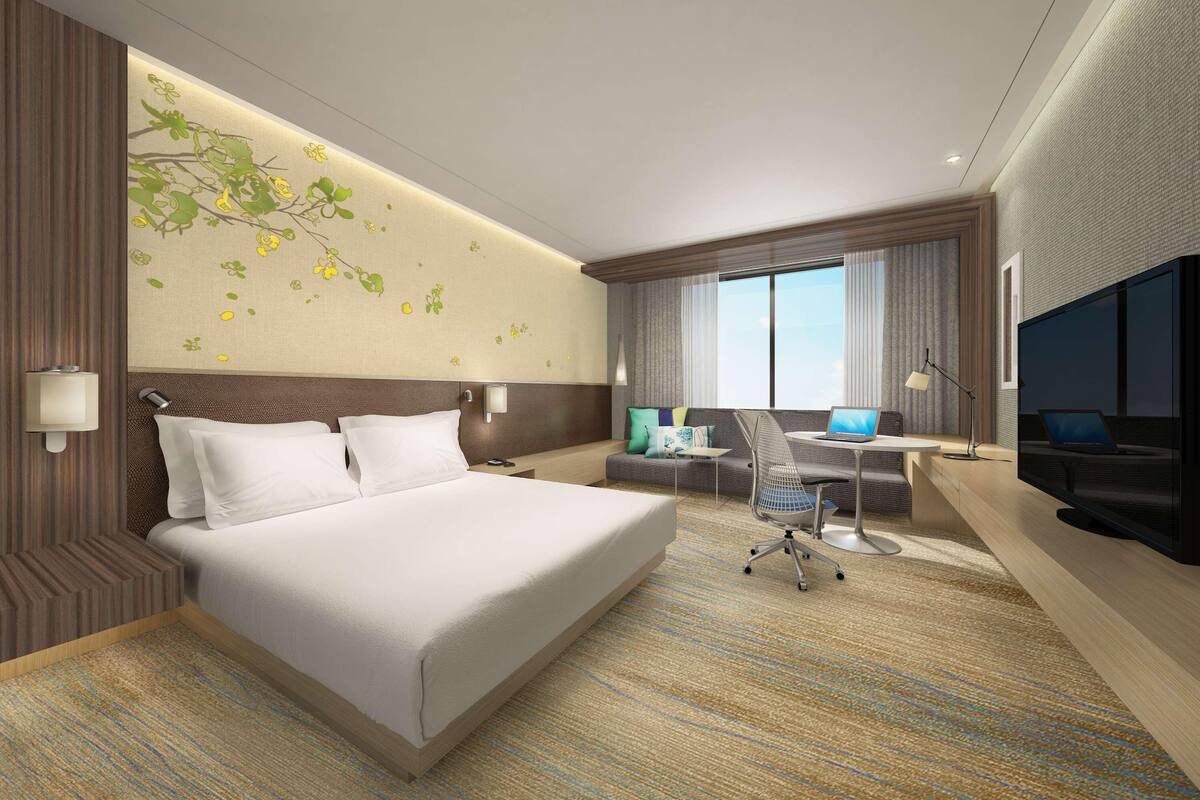 A modern hotel room with a large bed, a desk with a laptop, a TV, and a window with curtains.
