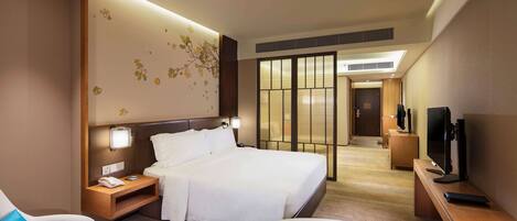 Una habitación de hotel con cama, mesitas de noche, televisión, escritorio y zona de estar.