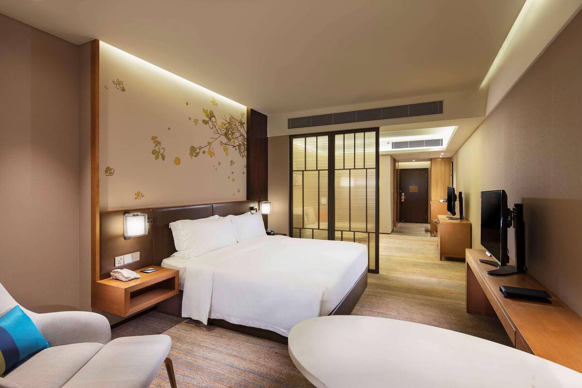 A hotel room with a bed, bedside tables, a TV, a desk, and a chair.