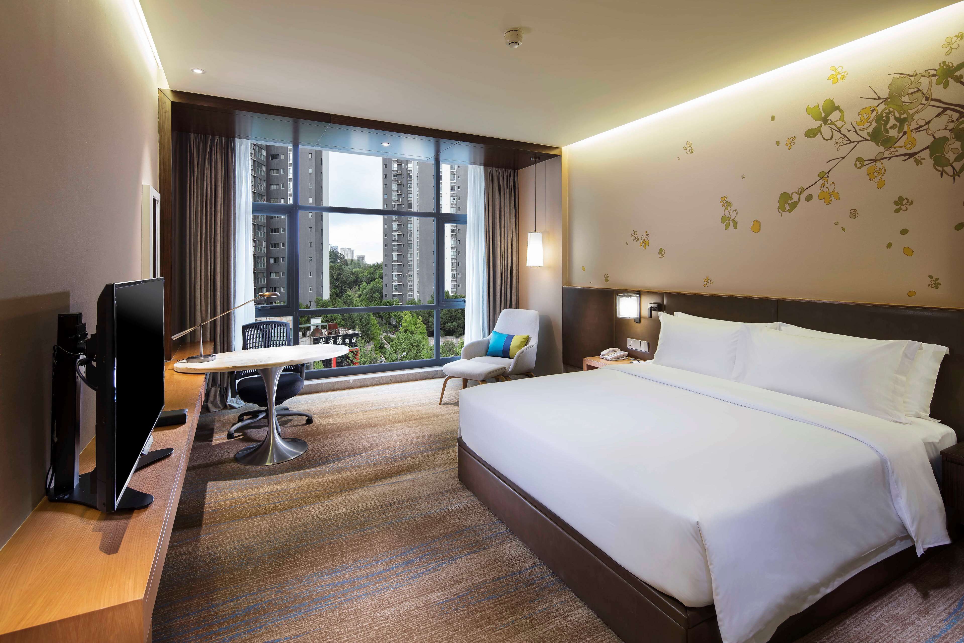 A hotel room with a large bed, a desk, a chair, and a TV.