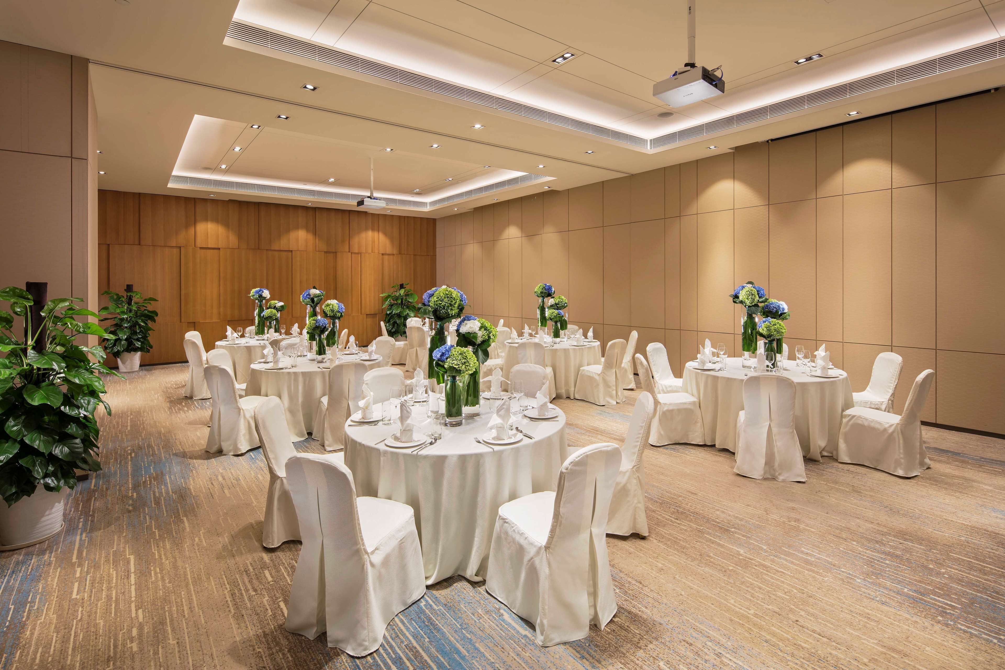Une salle de conférence avec des tables rondes, des chaises blanches et des arrangements floraux en guise de décoration centrale.
