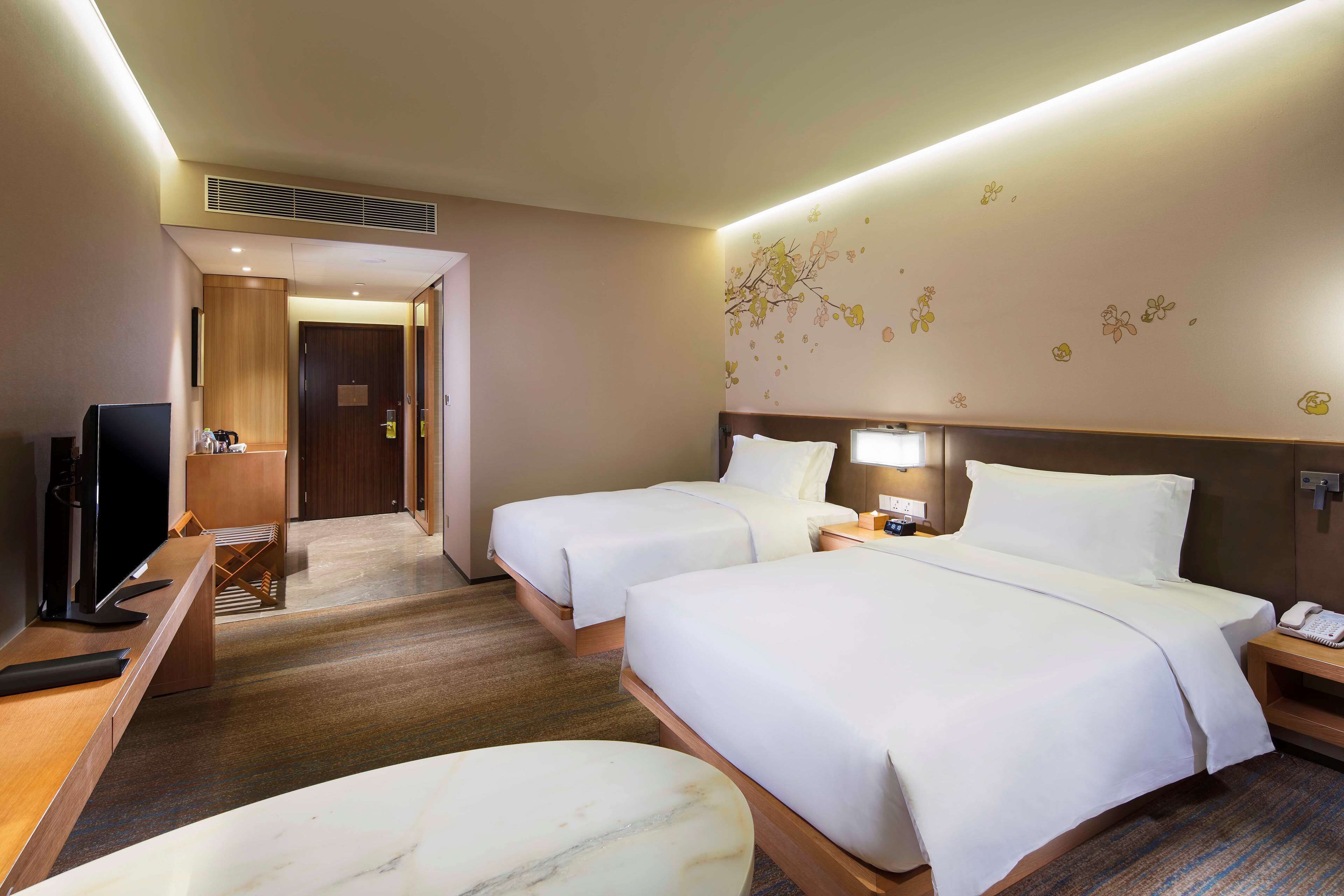 Une chambre d’hôtel avec deux lits, un bureau avec une télévision, un petit coin salon et une salle de bain visible à travers une porte ouverte.