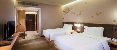 A hotel room with two beds, a desk with a TV, a small seating area, and a bathroom visible through an open door.