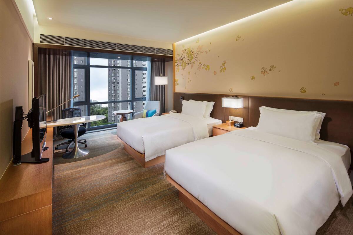 A hotel room with two beds, a desk, and a chair.
