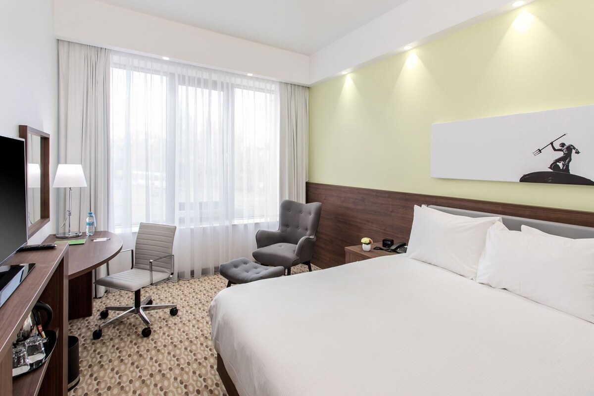 Ein Hotelzimmer mit Bett, Schreibtisch mit Stuhl, Fernseher, Lampe und einem Gemälde an der Wand.